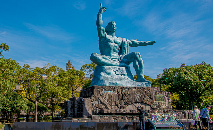 This is the ten foot high Peace Statue created by Seibo Kitamura for the Nagasaki Peace Park.  The right hand points to the threat of nuclear weapons, the left hand symbolizes eternal peace. The mild face, symbolizing divine grace, has eyes gently closed in prayer for the repose of the bomb victim's souls. The folded right leg signifies meditation and the left leg stands ready to help people of the world.
The statue is a mixture of Western and Eastern art, religion and ideology.PHOTO; ANGROVE