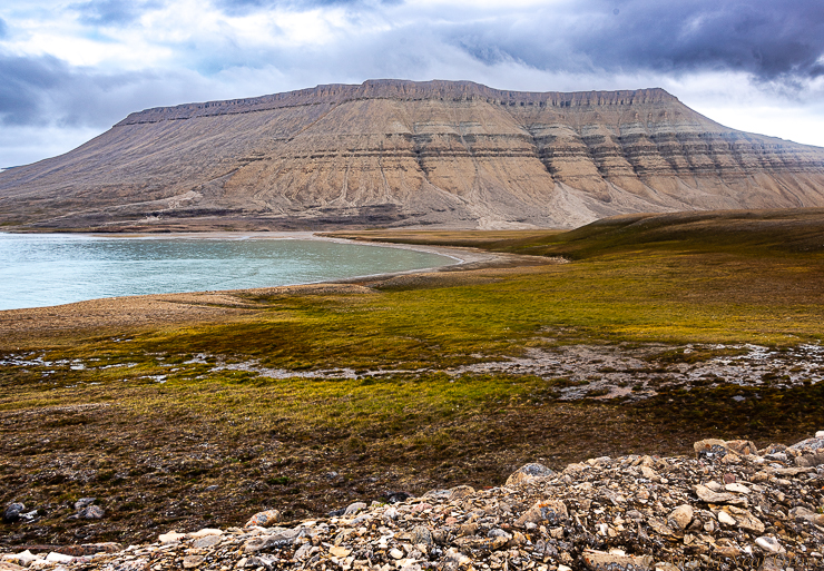 Northwest Passage Arctic Adventure:  Fijord on the south of Devon Island. Here the massive sedimentary rock cliffs soar above the water. In the foreground is the tundra where we hiked, searched for tiny flowers and looked for wildlife.  //PHOTO ANGROVE